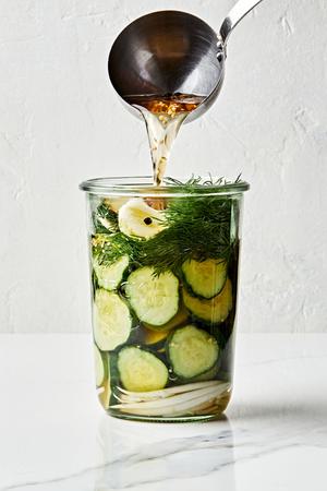 homemade brine being poured into a jar full of sliced onions, cucumbers, dill and garlic to make homemade dill pickles