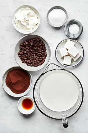 whole milk, sugar, cocoa powder, salt, vanilla, semi-sweet chocolate chips, whipped cream and marshmallows in bowls