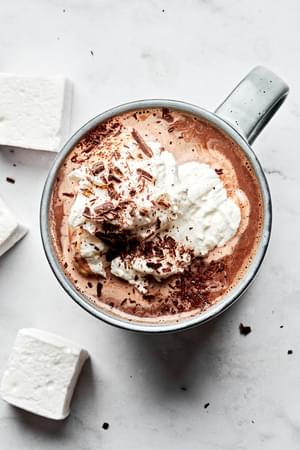 homemade hot chocolate topped with whipped cream and chocolate chips served with marshmallows
