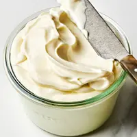 homemade mayonnaise in glass jar being scooped with a knife