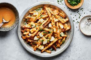homemade poutine in a silver pie plate next to bowl of gravy, salt and parsley for serving