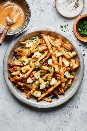 homemade poutine in a silver pie plate next to bowl of gravy, salt and parsley for serving