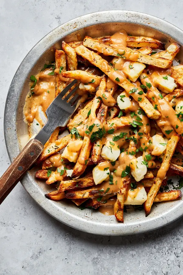 homemade poutine in a silver pie plate with a fork made with homemade fries topped with cheese curds and homemade gravy