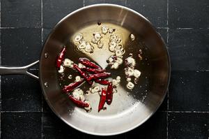 vegetable oil, sesame oil, garlic, chili peppers and peppercorn being heated together in a skillet
