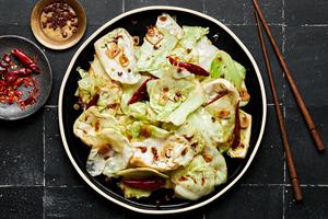 homemade hot and sour cabbage on a serving platter next to bowls of chili peppers and Sichuan peppercorns