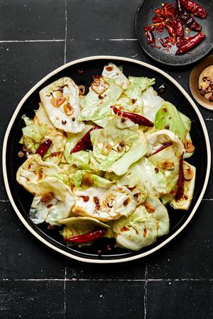 hot and sour cabbage on a serving platter next to bowls of chili peppers and Sichuan peppercorns