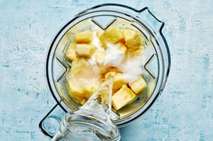 water being poured into a blender with diced pineapple and sugar to make homemade pineapple aqua fresca