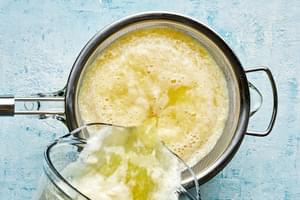 homemade pineapple agua fresca being poured out of a blender through a sieve into a drink pitcher