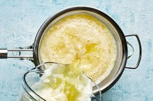 homemade pineapple agua fresca being poured out of a blender through a sieve into a drink pitcher
