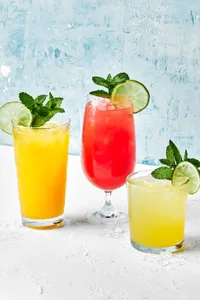 3 glasses of watermelon, mango and pineapple agua frescas garnished with fresh mint sprigs and lime wedges