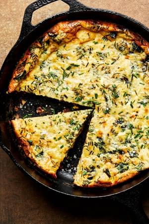 a homemade frittata in a cast iron skillet with a slice cut out made with milk, eggs, cheese, herbs, spices and cheese