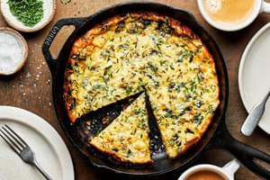 a homemade frittata in a cast iron skillet with a slice cut out made with milk, eggs, cheese, herbs, spices and cheese