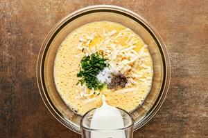 cream being poured into a bowl with beaten eggs, cheese, basil, salt and pepper to make a frittata