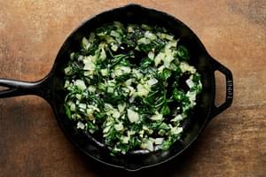 onion, garlic and veggies being cooked in olive oil in a cast iron skillet to make a frittata