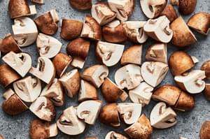 raw cremini mushrooms trimmed and quartered on the counter to amen roasted mushrooms