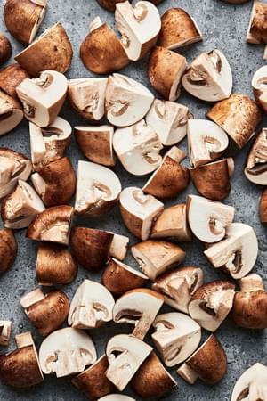 raw cremini mushrooms trimmed and quartered on the counter to amen roasted mushrooms