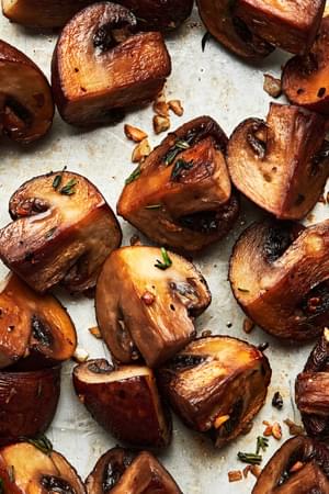 roasted cremini mushrooms seasoned with olive oil, salt, pepper, garlic cloves and fresh thyme on a baking sheet