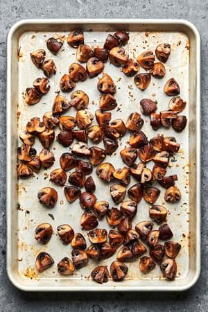 roasted cremini mushrooms seasoned with olive oil, salt, pepper, garlic cloves and fresh thyme on a baking sheet