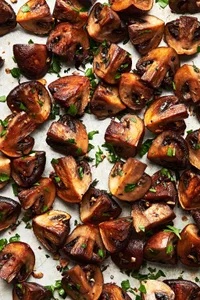 roasted cremini mushrooms seasoned with olive oil, salt, pepper, garlic cloves and fresh thyme on a baking sheet
