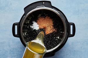 chicken stock being poured into an instant pot with sautéd onions, dried black beans, water, salt, and taco seasoning
