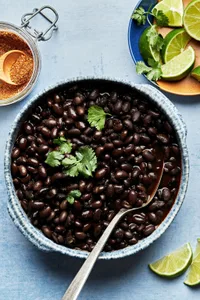 homemade black beans in a bowl topped with cilantro with a spoon, next to bowl of lime wedges and taco seasoning