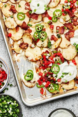 Irish nachos on a baking sheet topped with mozzarella, bacon, pico de Gallo, jalapeno, green onion and sour cream