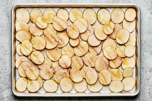thinly sliced potatoes on a baking sheet drizzled with olive oil and sprinkled with garlic, onion and chili powders and salt