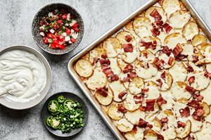 Irish nachos with mozzarella and bacon on a baking sheet next to bowls of sour cream, pico de Gallo and sliced jalapeños