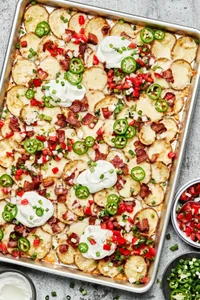Irish nachos on a baking sheet topped with mozzarella, bacon, pico de Gallo, jalapeno, green onion and sour cream