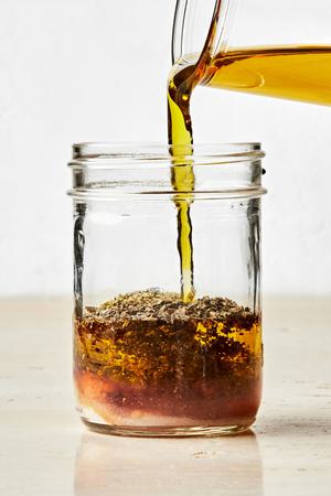 olive oil being poured into a jar with garlic powder, oregano, dried basil, salt and red wine vinegar