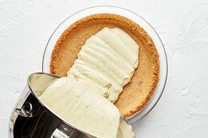 key lime pie filling being poured into a pre-baked homemade graham cracker crust in a glass pie pan