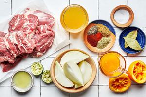 lamb shoulder, chicken stock, onion, orange and lime juice, spices and bay leaves in bowls on the counter to make lamb tacos
