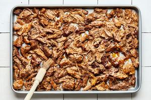 shredded lamb, carnitas-style, on a baking sheet being brushed with reserved cooking juices ready to be crisped in the oven