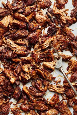 homemade shredded lamb, carnitas-style, on a baking sheet after being crisped in the oven being scooped with a fork