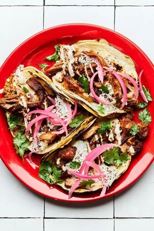 three homemade lamb tacos on a plate topped with cilantro, tahini and tzatziki sauces, sumac and pickled onions