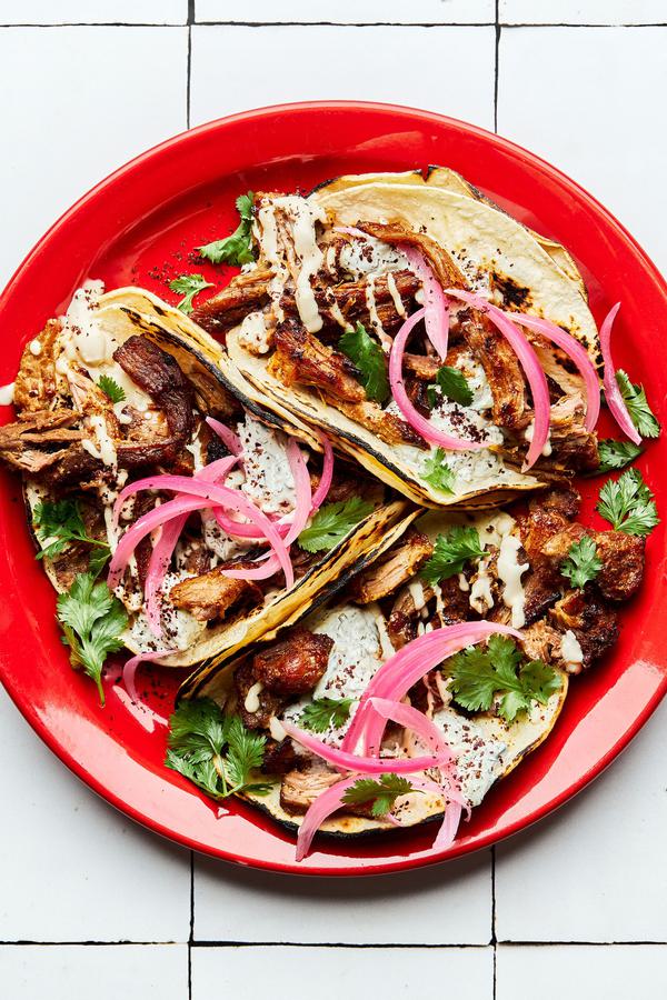 three homemade lamb tacos on a plate topped with cilantro, tahini and tzatziki sauces, sumac and pickled onions