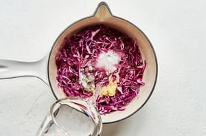 water being poured over red cabbage, apple cider and red wine vinegars, sugar & seasonings in a pan for pickled red cabbage