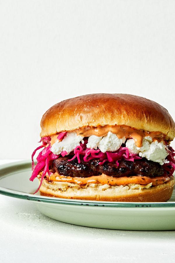 A Lamb Burger With Harissa Mayo, Pickled Red Cabbage and chèvre cheese on a brioche bun on a plate on the counter
