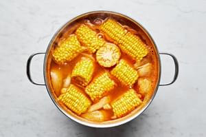 onions, potatoes and corn boiling in a pot of water, chicken stock smashed garlic and old bay seasoning