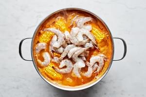 shrimp, onions, potatoes and corn boiling in a pot of water, chicken stock smashed garlic and old bay seasoning