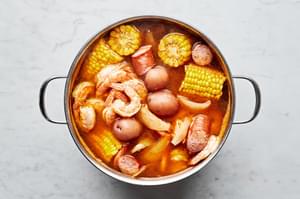 shrimp, sausage, onions, potatoes and corn boiling in a pot of water, chicken stock smashed garlic and old bay seasoning