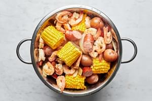 homemade low country boil in a strainer pot with corn, sausage, shrimp, potatoes and onions