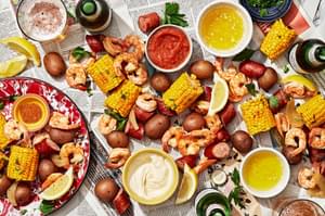 low country boil made with corn, shrimp, potatoes and sausage spread out on a table with sauces for dipping