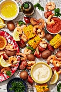 low country boil made with corn, shrimp, potatoes and sausage spread out on a table with sauces for dipping