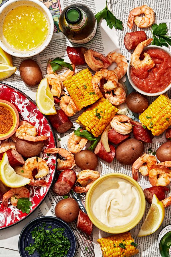 low country boil made with corn, shrimp, potatoes and sausage spread out on a table with sauces for dipping