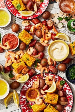 low country boil made with corn, shrimp, potatoes and sausage spread out on a table with sauces for dipping