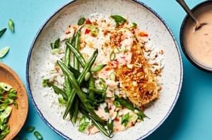 A macadamia nut crusted fish bowl with coconut rice, green beans and a sweet chili mayo sauce drizzled on top