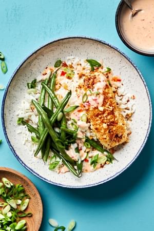 A macadamia nut crusted fish bowl with coconut rice, green beans and a sweet chili mayo sauce drizzled on top