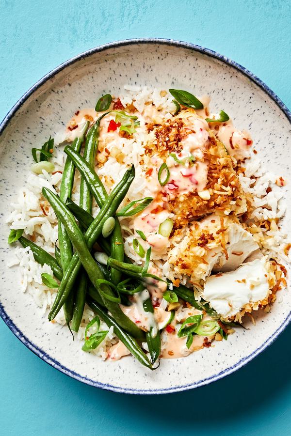 A macadamia nut crusted fish bowl with coconut rice, green beans and a sweet chili mayo sauce drizzled on top