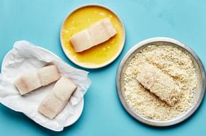 raw fish being dipped into a bowl of beaten eggs and then into a bowl of macadamia nuts and coconut to make crusted fish